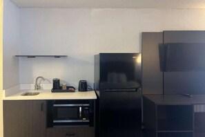 Una cocina compacta equipada con un lavamanos, un microondas, una cafetera y un refrigerador.