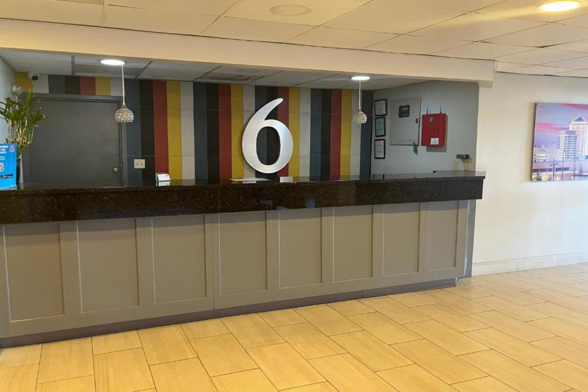 A reception desk with a large number 6 sign, a red fire extinguisher, and a cityscape view.