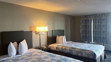 A hotel room with two beds, a nightstand, a lamp, and a patterned curtain.