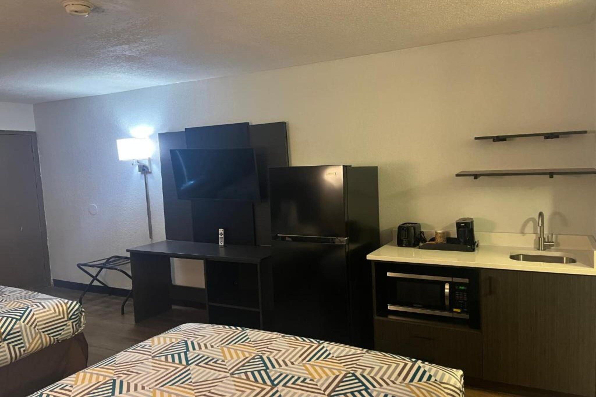 Habitación de hotel con cama, escritorio, televisión de pantalla plana, refrigerador, microondas y cafetera.