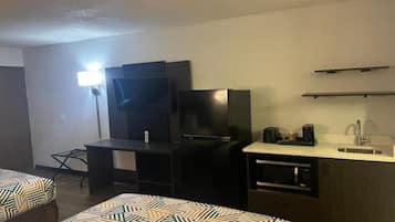 Habitación de hotel con cama, escritorio, televisión de pantalla plana, refrigerador, microondas y cafetera.