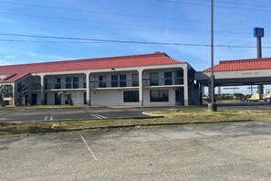 Ein zweistöckiges Motel mit rotem Dach, einem Parkplatz und einer Tankstelle im Hintergrund.