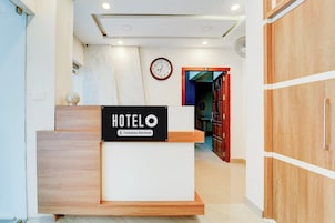 Un mostrador de recepción de hotel con un letrero que indica servicio empresarial. Hay un reloj en la pared y una puerta que da a otra habitación.
