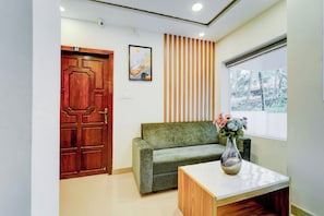 A reception area with a wooden door, a sofa, a small table with a vase, and a window with a view of trees.