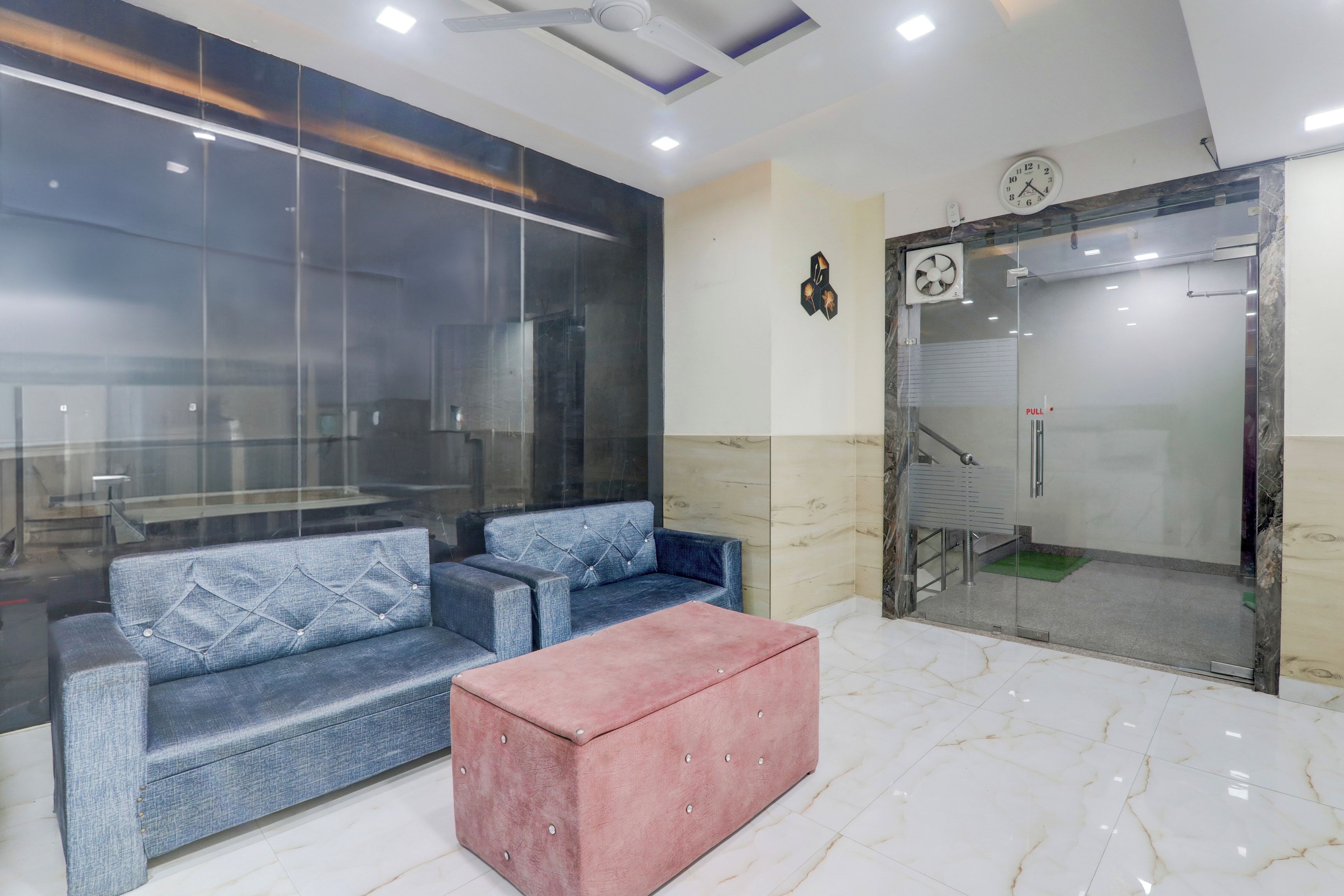 A modern lobby with a seating area, a clock, and a glass elevator.