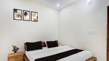 Une chambre à coucher avec un lit en bois, une literie blanche, une table de chevet ornée d’un vase et trois œuvres d’art encadrées accrochées au mur.