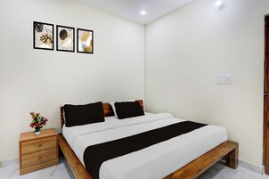 A bedroom with a wooden bed, white bedding, a nightstand with a vase, and three framed artworks on the wall.