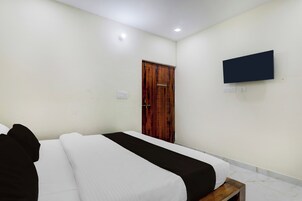 Habitación de hotel con cama, puerta de madera, televisor montado en la pared y una mesita de noche pequeña.