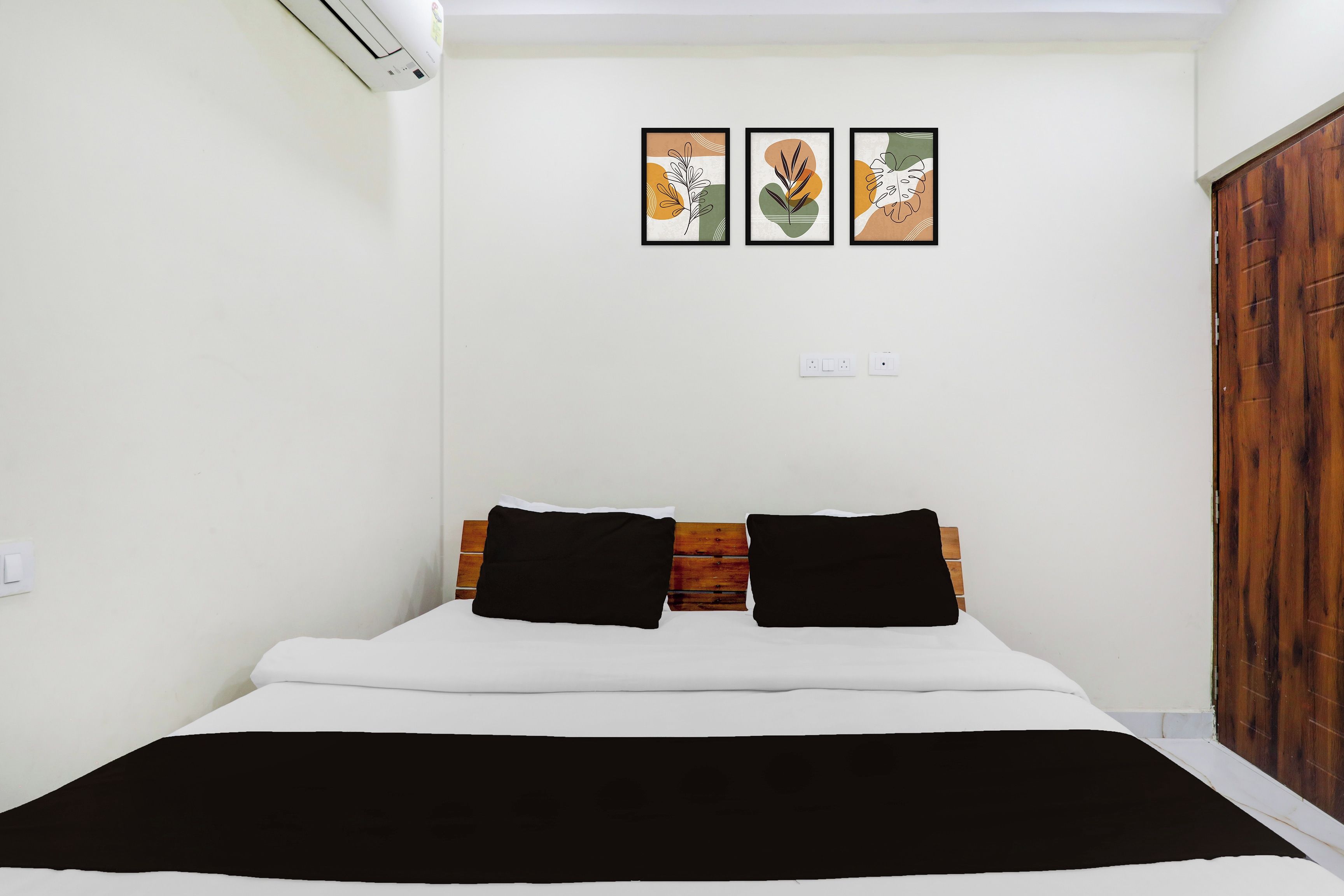 A bedroom with a bed, two black pillows, a white bedspread, and a black blanket. There are three framed artworks on the wall.