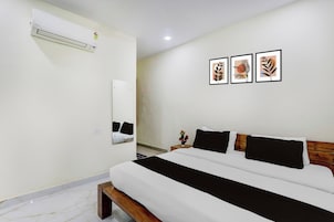 Habitación de hotel con una cama, una mesita de noche, un espejo, un aire acondicionado y tres cuadros enmarcados en la pared.