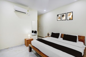 Habitación de hotel con cama, mesita de noche, lámpara, aire acondicionado y un cuadro colgado en la pared.