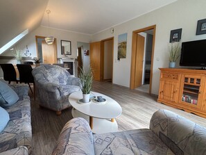 A modern living room with a sofa, armchair, and a television. - Jacobihof - Fiete - Jacobihof "Fiete" 3-room apartment near the beach in a quiet (Dahme)