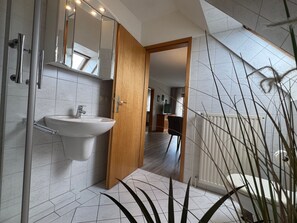 A modern bathroom with a white sink, a wooden door, and a mirror. - Jacobihof - Fiete - Jacobihof "Fiete" 3-room apartment near the beach in a quiet (Dahme)