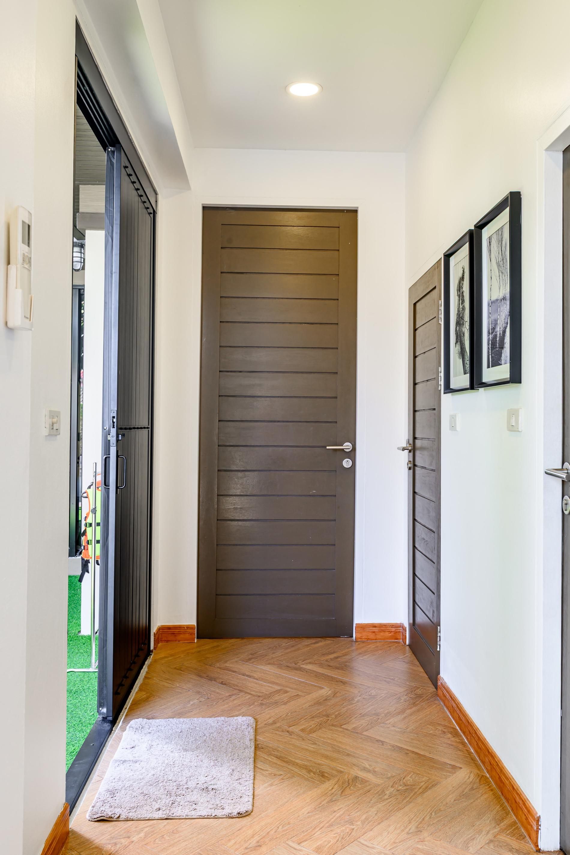 Un pasillo con piso de madera, una puerta gris y una pared blanca con cuadros enmarcados.