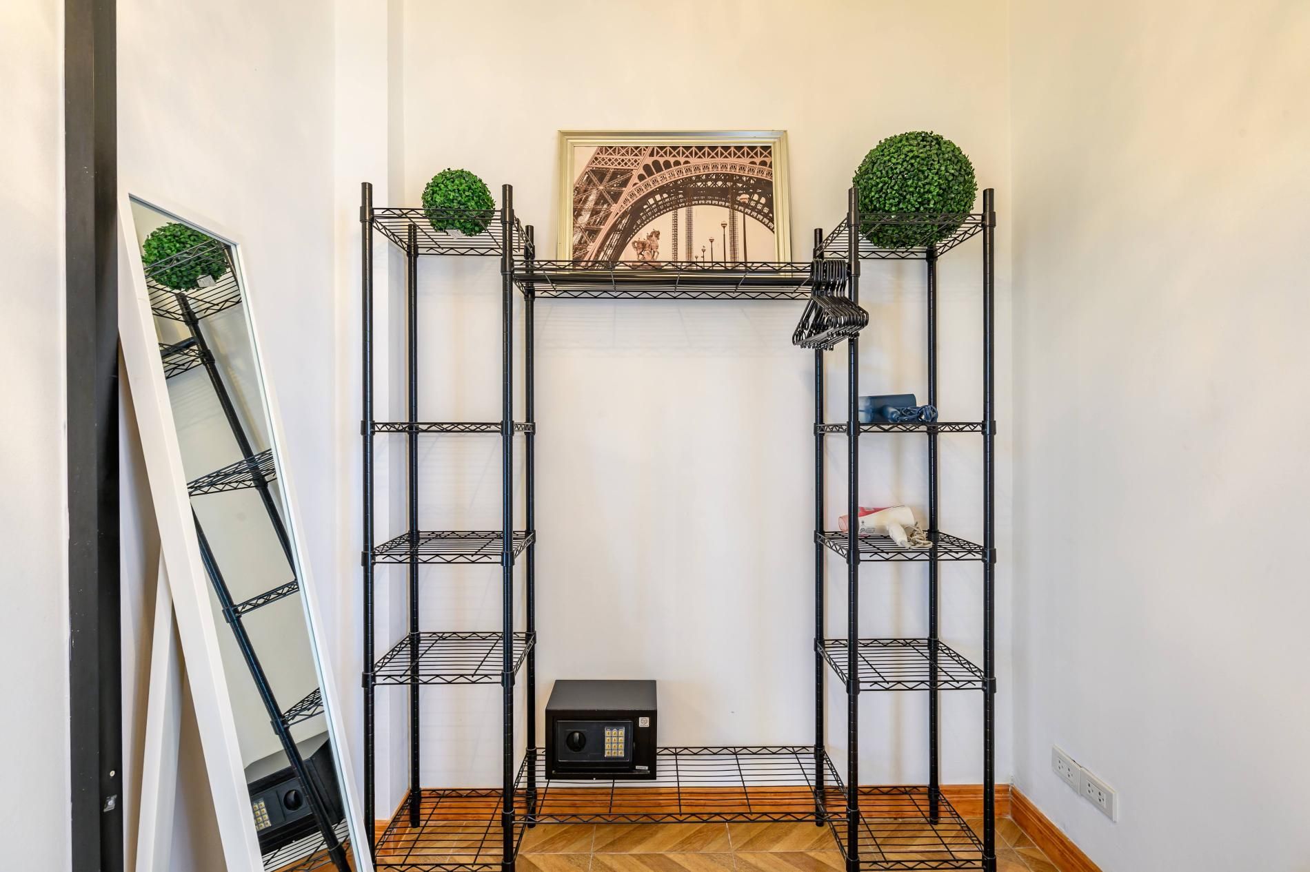 A room with a black metal shelving unit against a white wall, a framed picture of the Eiffel Tower, and a small heater on the floor.