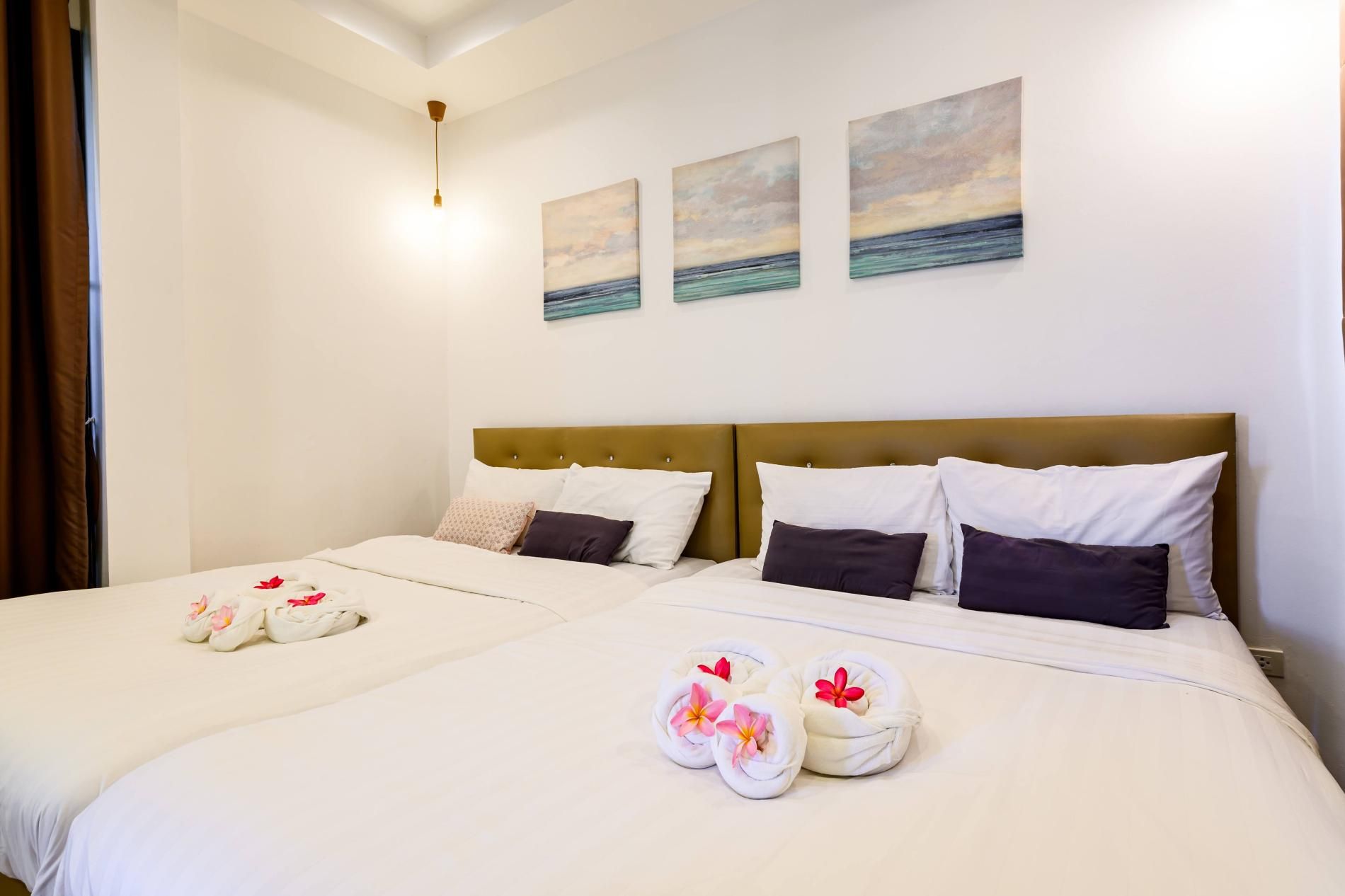 Habitación de hotel con dos camas, cada una con sábanas y almohadas blancas, y toallas con flores. Hay tres cuadros en la pared que representan paisajes.