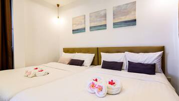 Habitación de hotel con dos camas, cada una con sábanas y almohadas blancas, y toallas con flores. Hay tres cuadros en la pared que representan paisajes.