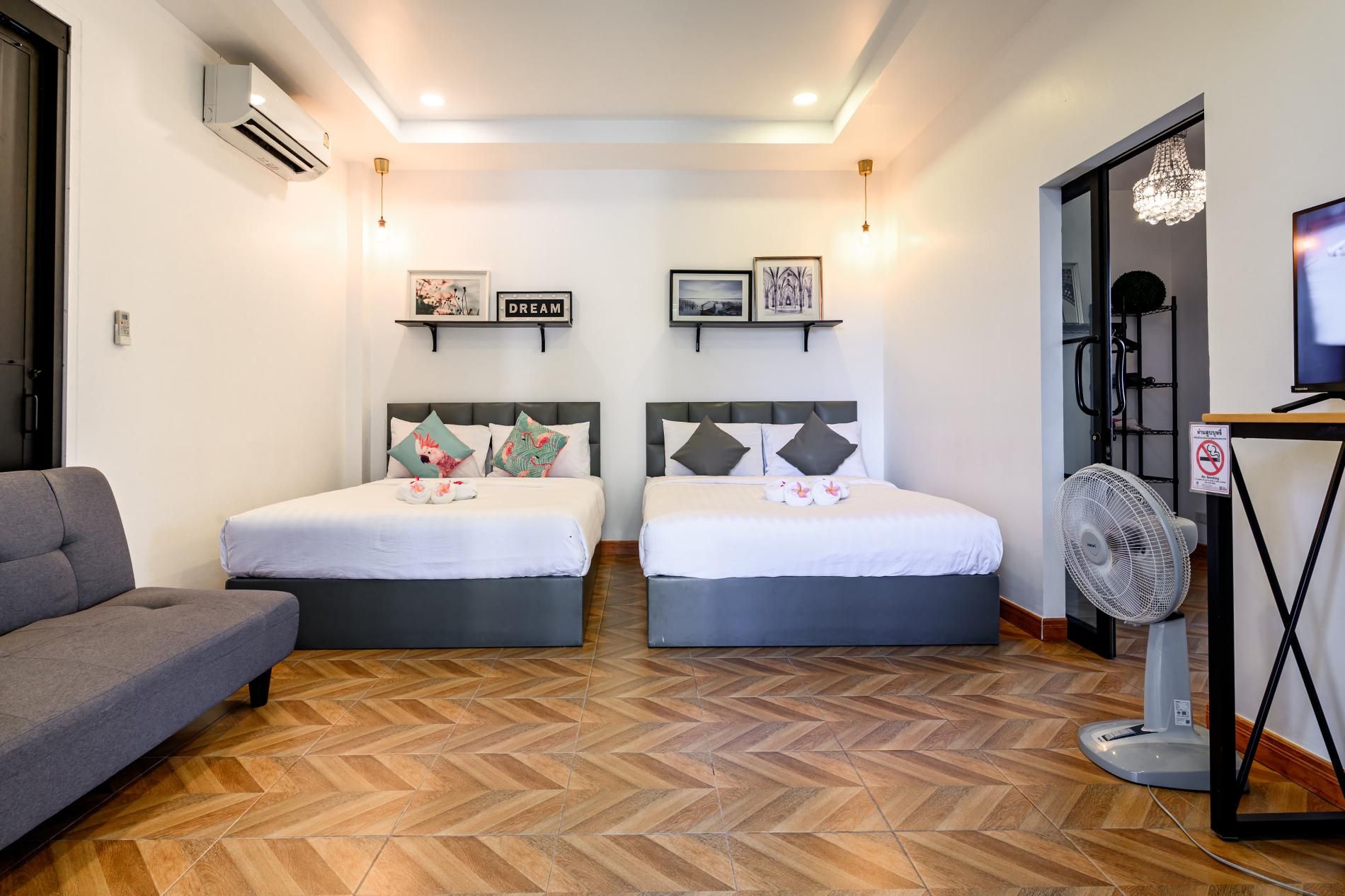 A hotel room with two beds, a grey sofa, a standing fan, and a television.