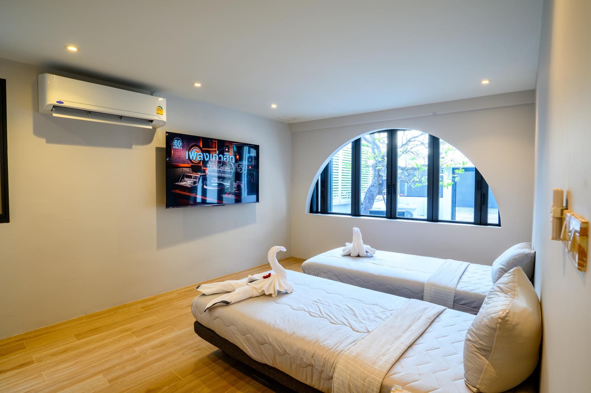 A hotel room with two beds, a flat-screen TV, an air conditioner, and a window with a view of the outside.