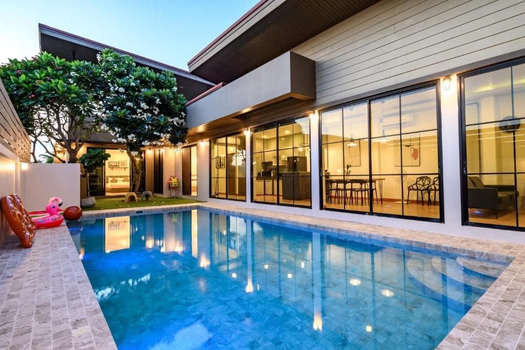 Une maison moderne dotée d’une piscine, de grandes fenêtres et de mobilier d’extérieur.