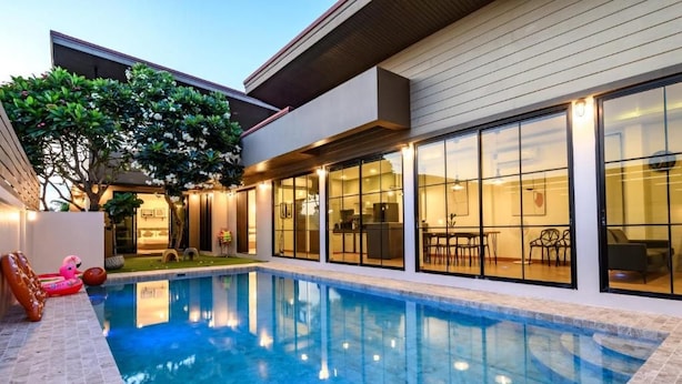 A modern house with a swimming pool, large windows, and outdoor furniture. - Modern Spacious 3 beds Pool Villa BA1 (Pattaya)