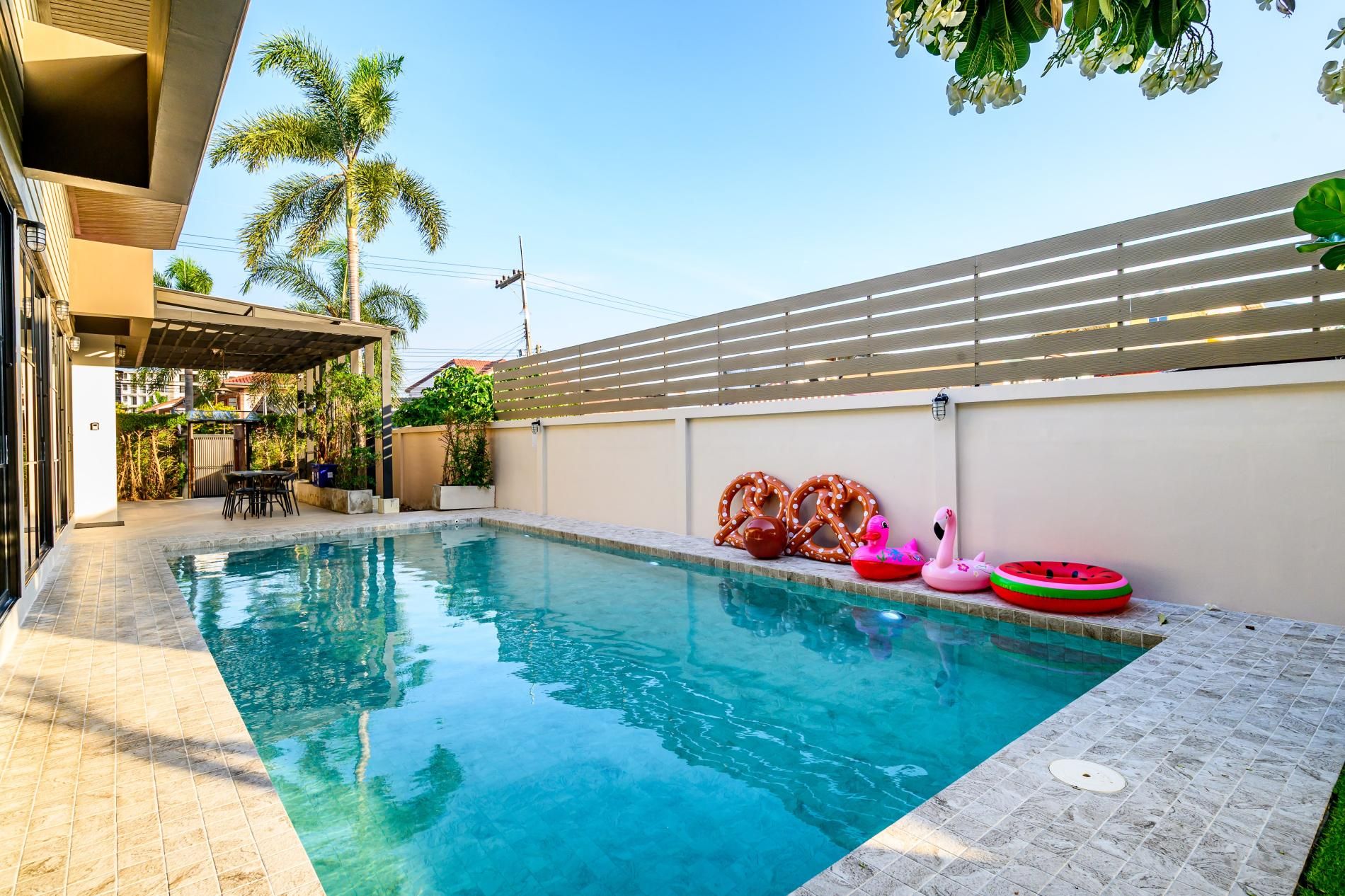 Una piscina con borde de azulejos, rodeada por una cerca y con juguetes inflables.