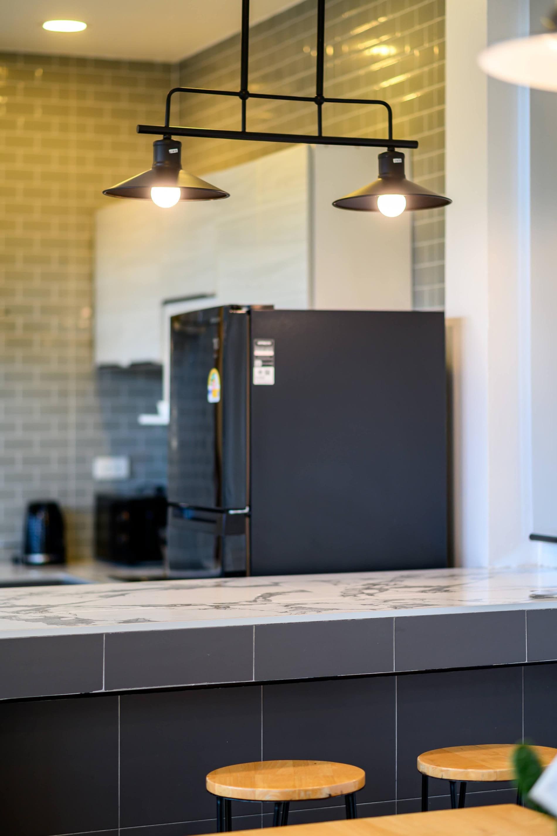 A modern kitchen with a black refrigerator, two pendant lights, and a marble countertop.