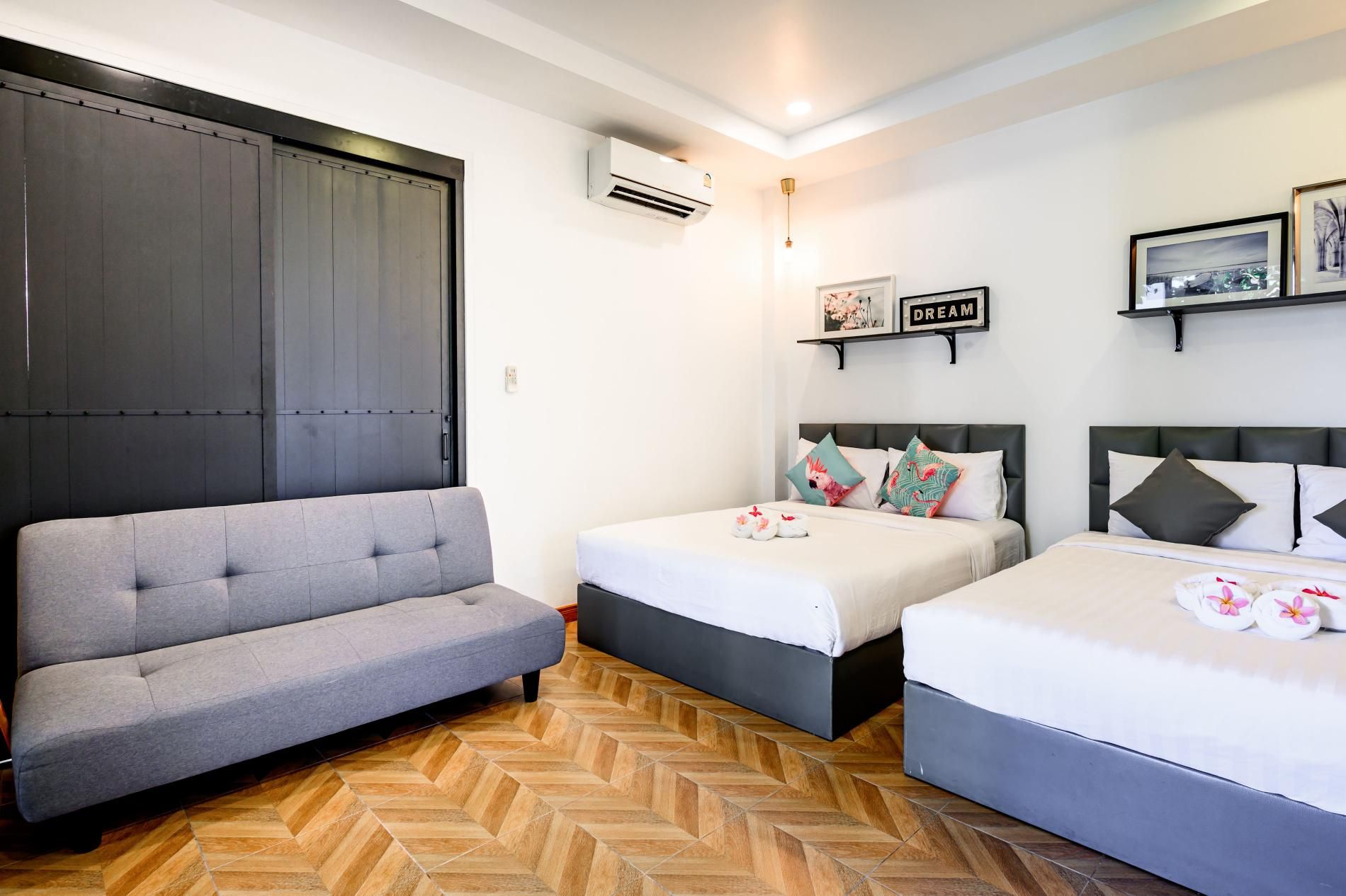 Habitación de hotel con sofá, dos camas, piso con estampado de espiga, unidad de aire acondicionado y obras de arte colgadas en la pared.