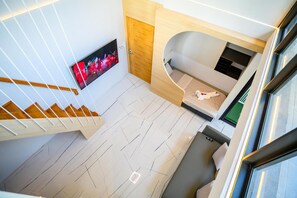 A modern hotel room with a staircase, a flat-screen TV, a bed with a headboard, and a small seating area. - Modern Spacious 3 beds Pool Villa BA1 (Pattaya)