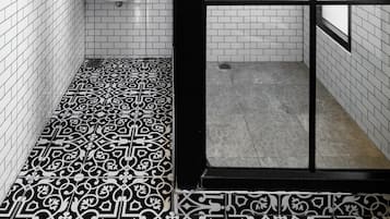 A bathroom with a white tiled wall, a round mirror, a sink, and a shower area with a glass door.