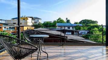 Una terraza techada con suelo de espiga, sillas metálicas y vistas a edificios y zonas verdes.