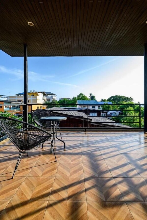 Una terraza techada con suelo de espiga, sillas metálicas y vistas a edificios y zonas verdes.