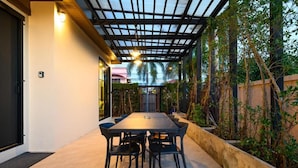 An outdoor dining area with a table and chairs, surrounded by plants and a pergola structure. - Modern Spacious 3 beds Pool Villa BA1 (Pattaya)