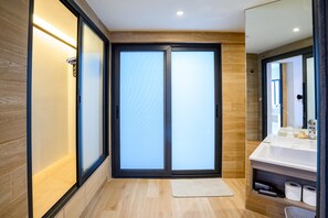 Une salle de bain moderne avec une porte coulissante en verre, un lavabo blanc et un plancher en bois.