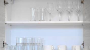 A white cabinet with two shelves containing clear glasses and white cups.