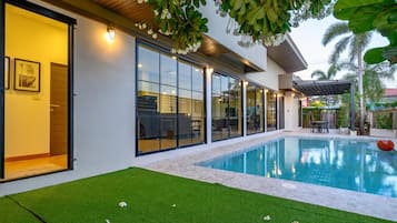 Una casa moderna con piscina, puertas de vidrio amplias y un área de patio.