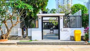 A modern building entrance with a black door, a small outdoor seating area, and a yellow trash bin. - Modern Spacious 3 beds Pool Villa BA1 (Pattaya)