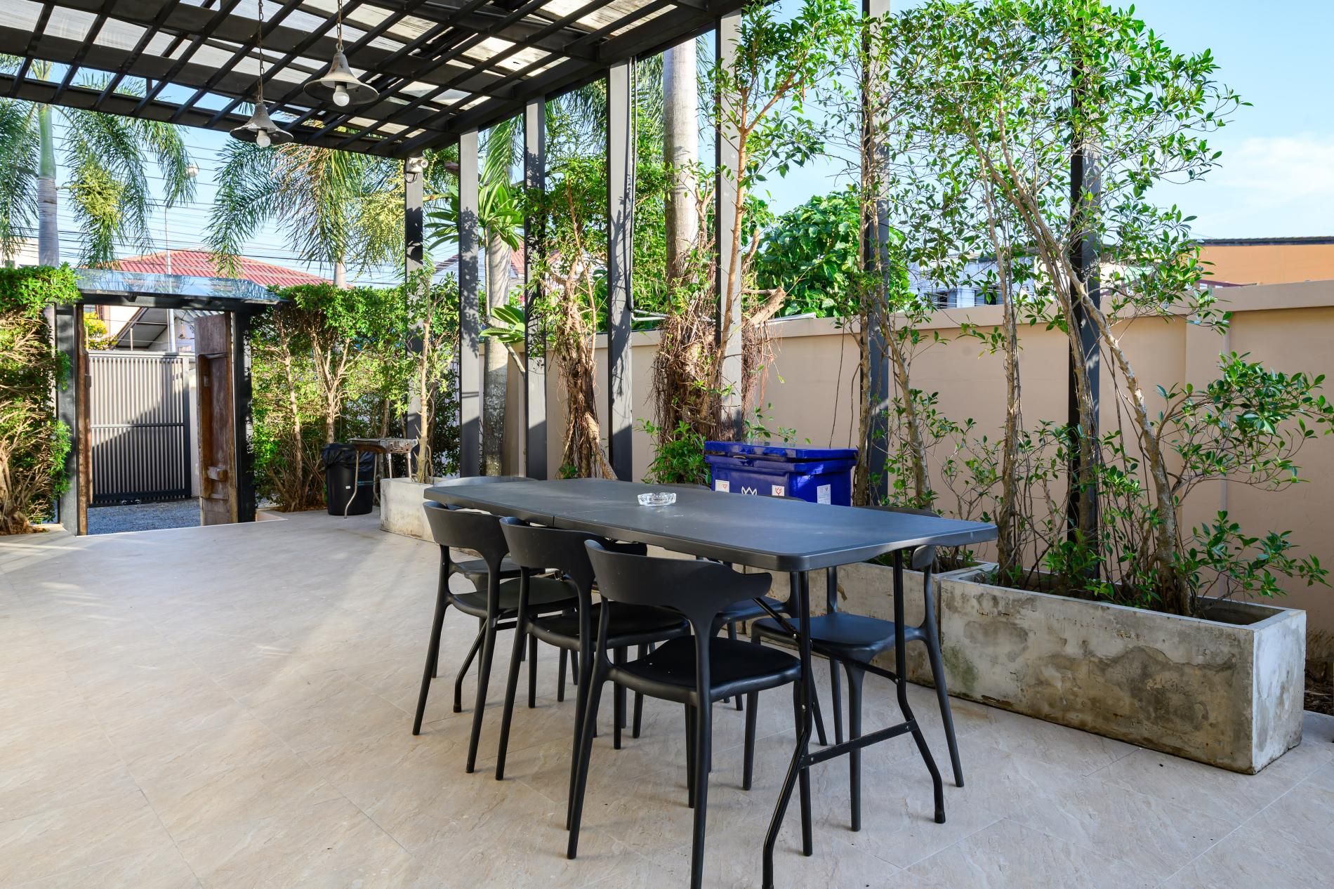 Un patio al aire libre con una mesa y sillas, rodeado de plantas y una pérgola.