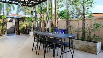 Un patio al aire libre con una mesa y sillas, rodeado de plantas y una pérgola.