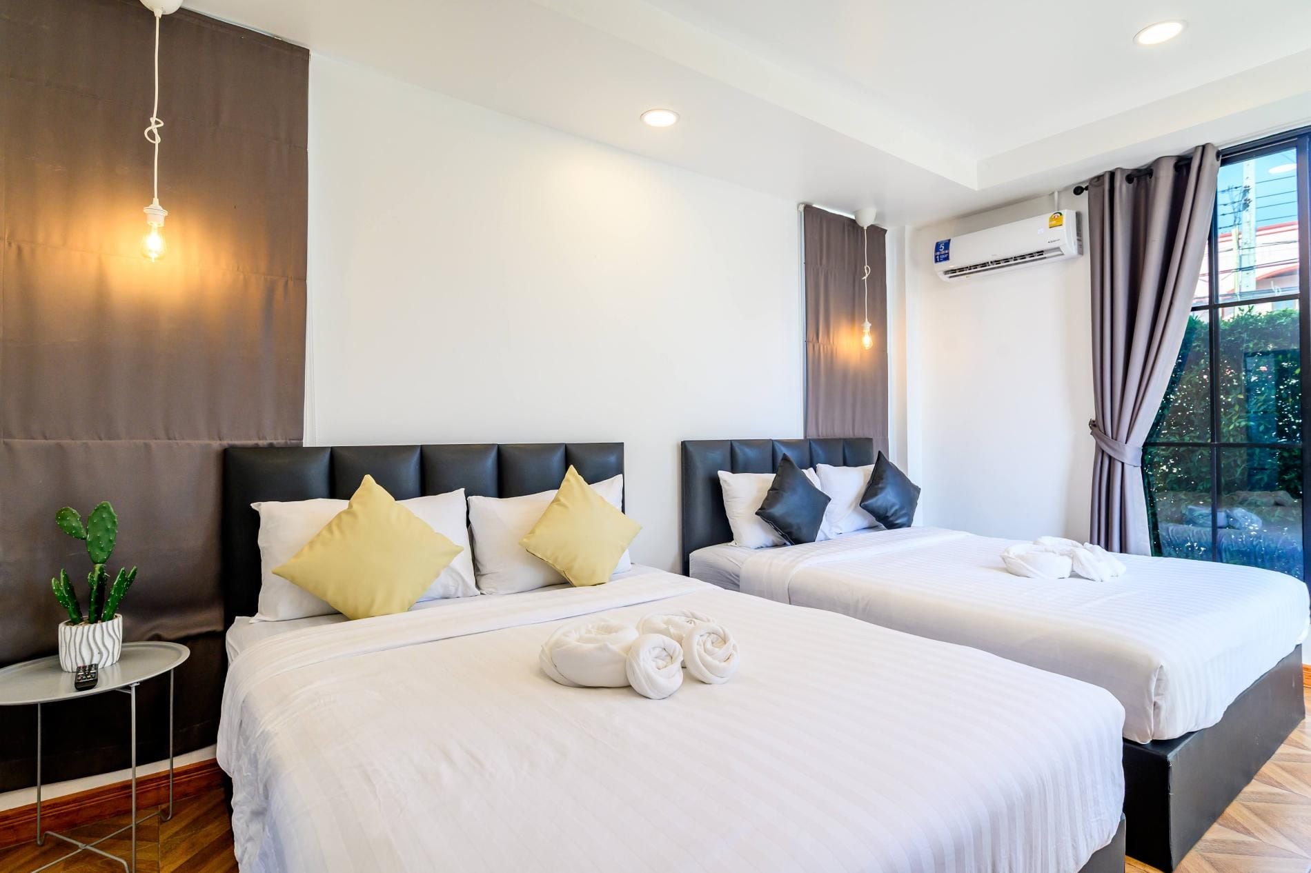 A hotel room with two beds, a potted plant, a small table, and an air conditioning unit.