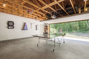 A spacious indoor area with a ping pong table, dartboard, and a small shelf with items. - Gilmore Lake Family Escape w/ Game Room & Dock! (Minong)
