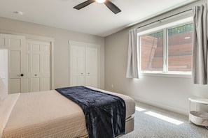 A bedroom with a bed, a ceiling fan, a window with curtains, and a door. - Gilmore Lake Family Escape w/ Game Room & Dock! (Minong)