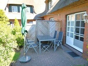An outdoor patio with a table and chairs, a green umbrella, and a brick wall. - Kiek Ut 9, Holiday Apartment 2 (Wyk auf Foehr)
