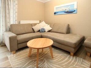 A beige sofa with a round wooden coffee table in a living room with patterned carpet. - Kiek Ut 9, Holiday Apartment 2 (Wyk auf Foehr)