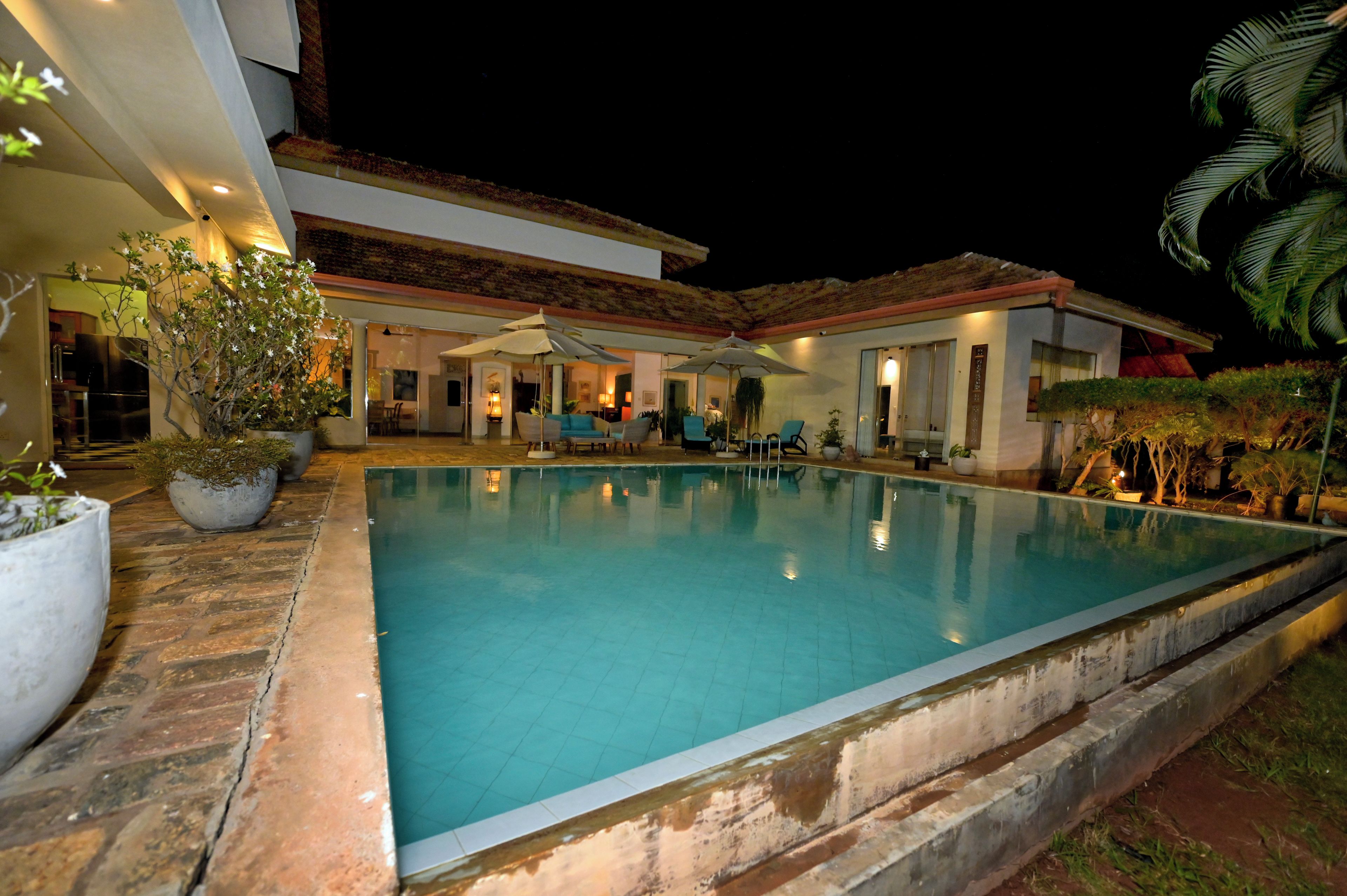 A swimming pool with a tiled deck, surrounded by potted plants and outdoor furniture.