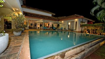 A swimming pool with a tiled deck, surrounded by potted plants and outdoor furniture.
