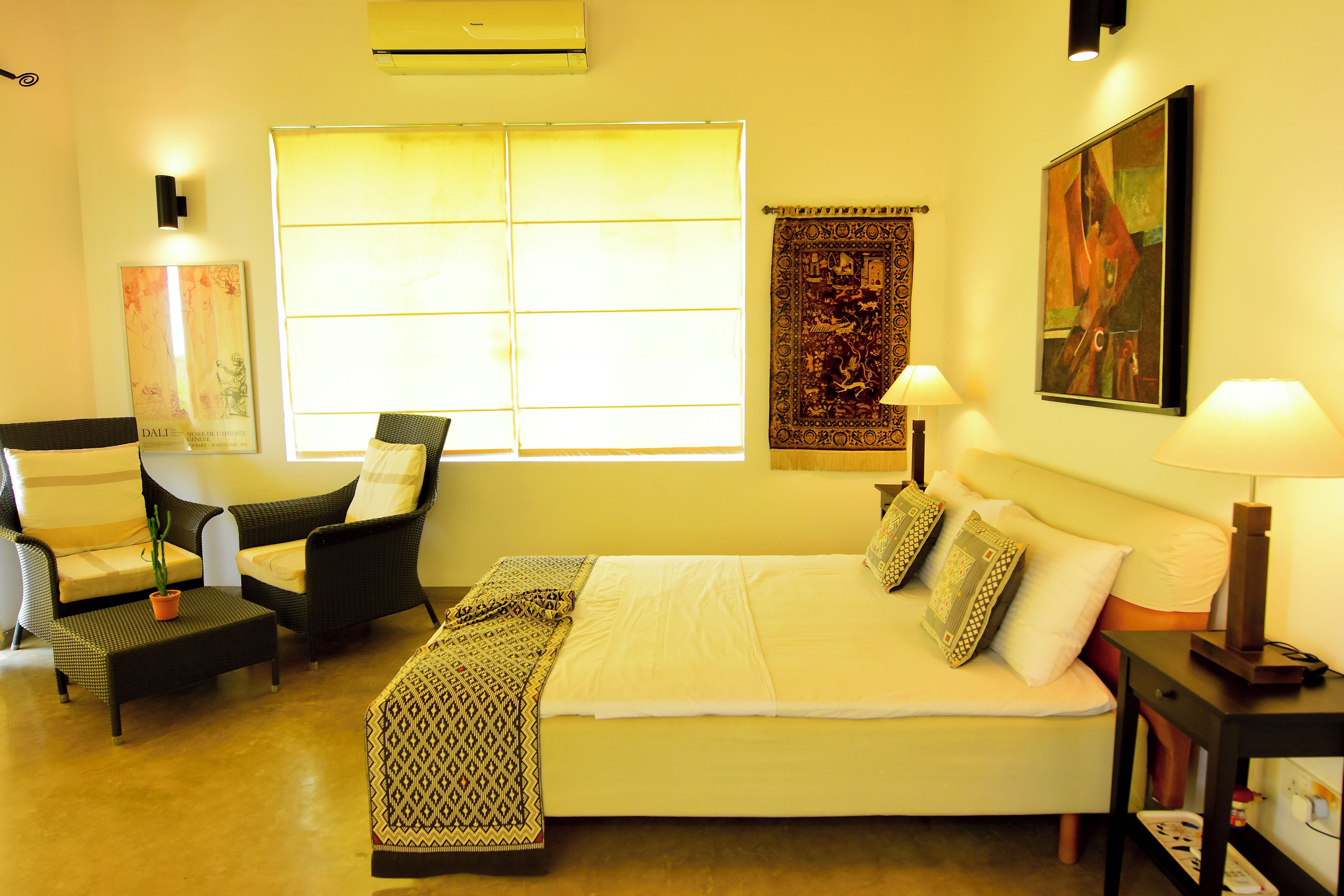 A hotel room with a bed, two chairs, a window, a painting, and a lamp.