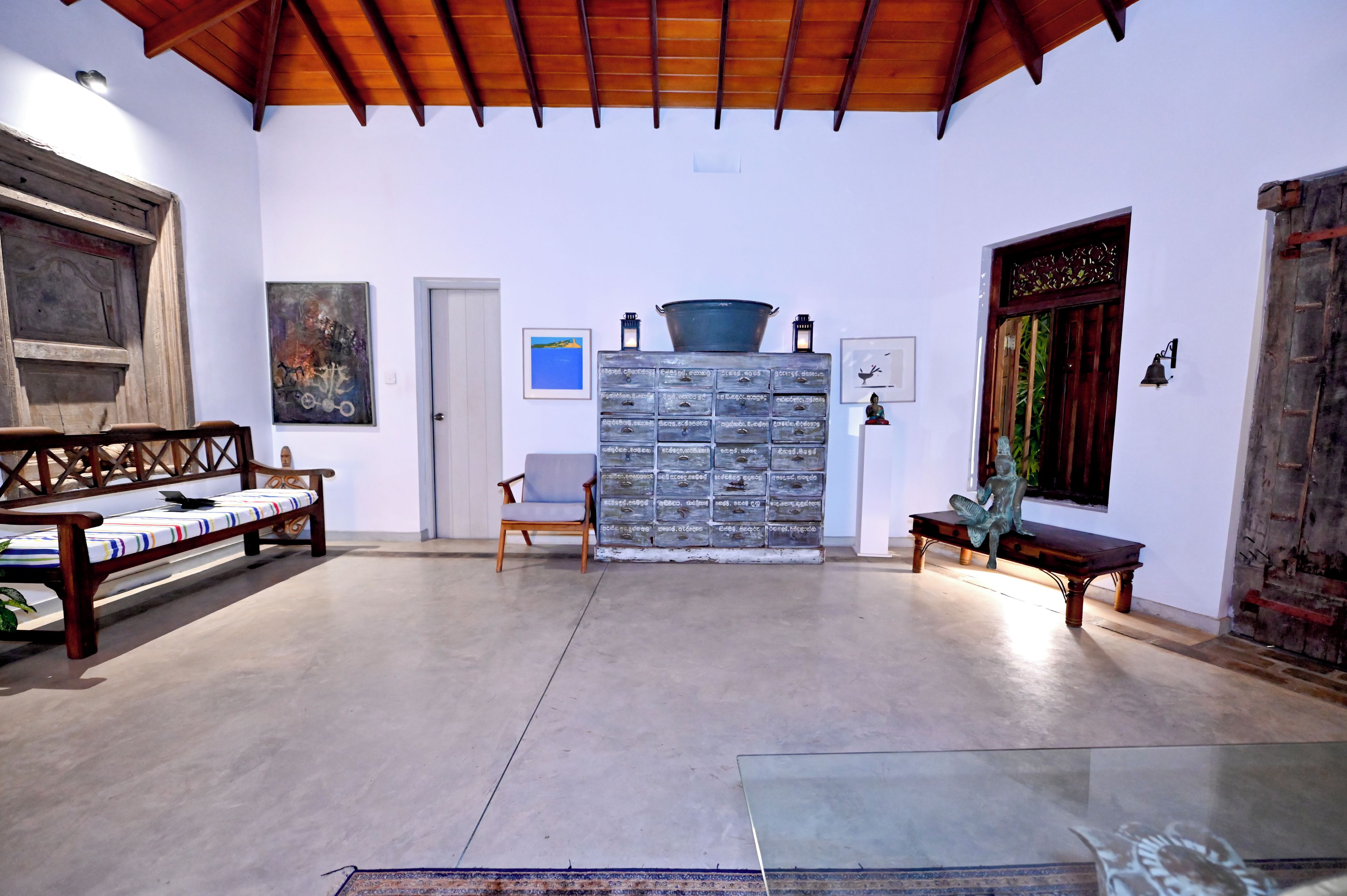 A spacious room with a high ceiling, a wooden bench, a chair, and a glass table.