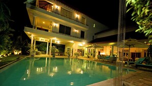 Un hotel de varios pisos con piscina, mobiliario exterior y una entrada bien iluminada.