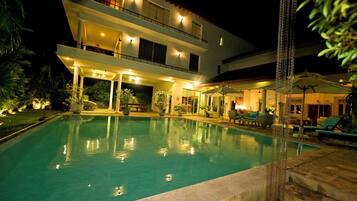 A multi-story hotel with a swimming pool, outdoor seating, and a well-lit entrance.